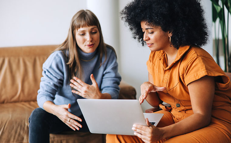 Two businesswomen having a discussion while looking at a laptop screen