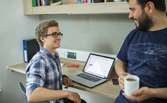 Male student in checked shirt chatting in room with friend