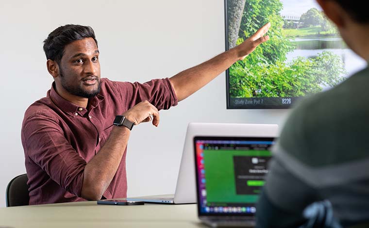 A student confidently addressing a group while pointing at a big screen