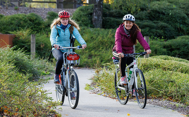 Tow university staff cycling through landscaped grounds