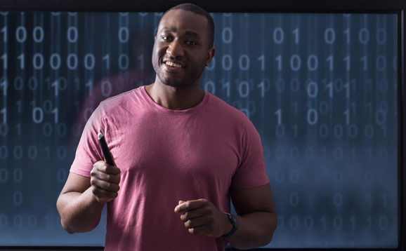 A man proudly presenting in front of a screen of ones and zeroes