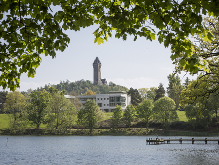 Airthrey Loch with the Wallace Monument visible. Leaves from a tree are coming into the frame.