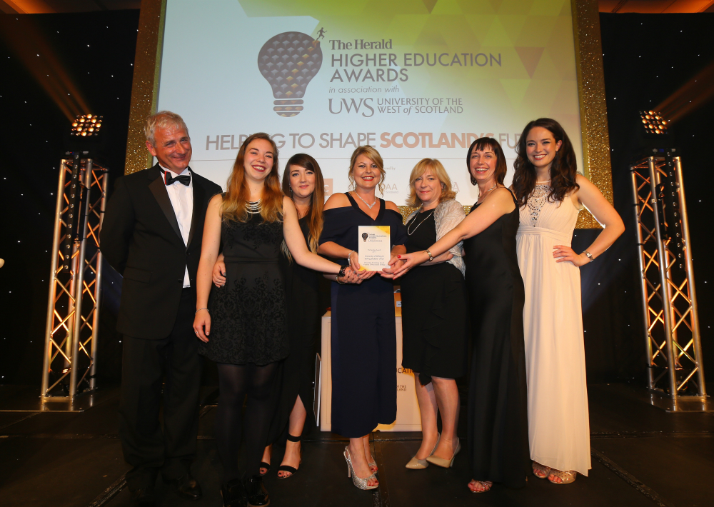 six women and one man standing on a stage holding their award