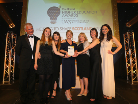 six women and one man standing on a stage holding their award 