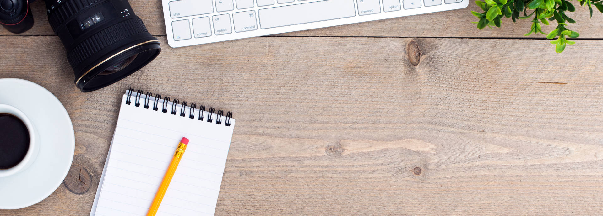 An image of a camera, keyboard, coffee and a notepad and pencil on a desk