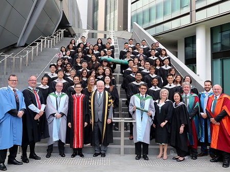 Senior staff and students in graduation robes standing on stairs