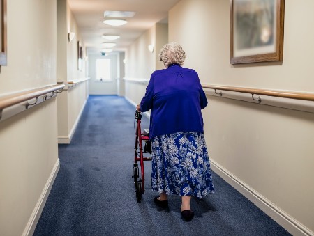 Elderly woman walks along hall using a walking frame