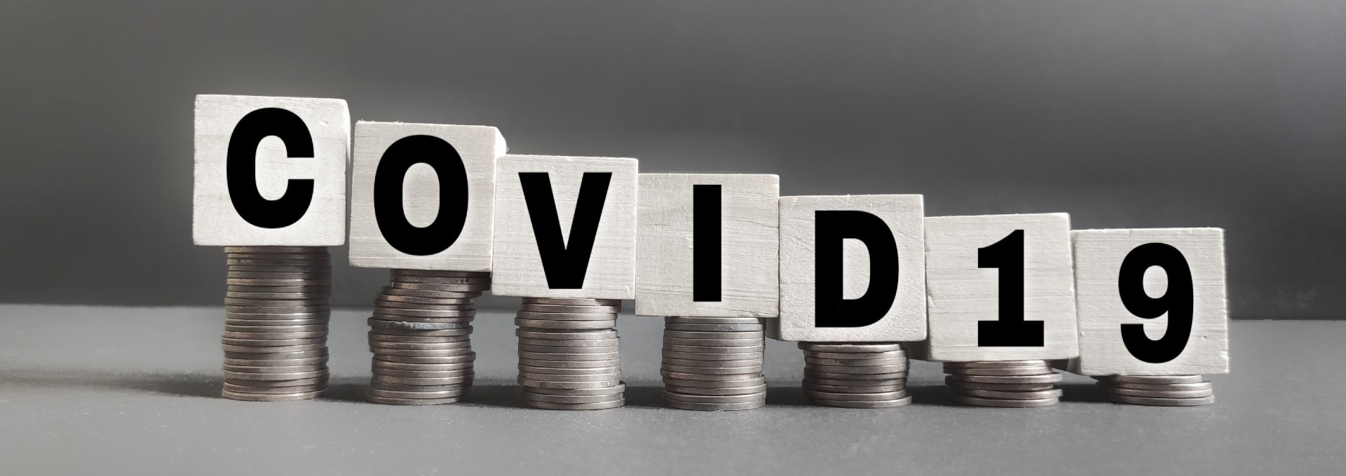 Five stacks of silver coins with the word COVID positioned in white blocks on top of the stacks