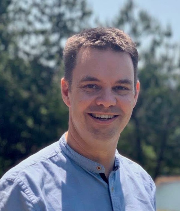 Photograph of Dr Edward Duncan - he is pictured wearing a blue shirt, smiling and looking straight to camera. The photo has been taken outside, and there are trees in the background