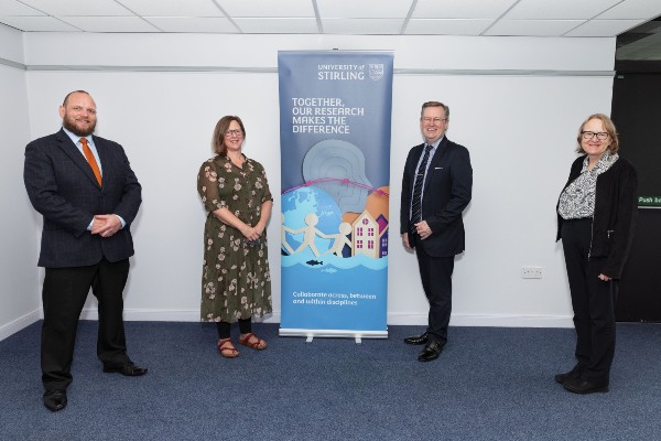 University of Stirling staff stand beside an advertising banner as they welcome MSP Alexander Stewart