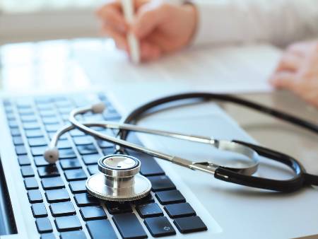 Stethoscope sits on top of a laptop keyboard in a GP's office