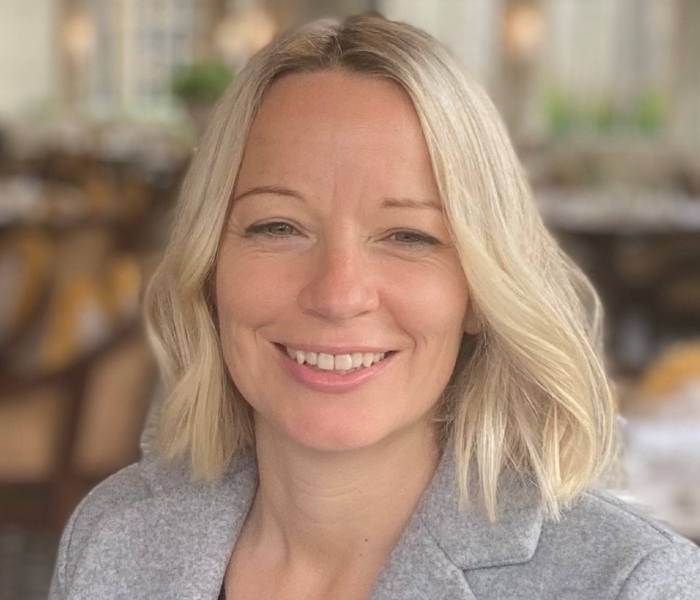 Portrait photograph of Dr Lynne Gilmour. She has shoulder length blonde hair and wears a grey blazer.