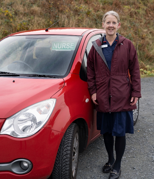 Nurse Helen Davies in her uniform beside her car which displays a sign saying 'Nurse' in the window