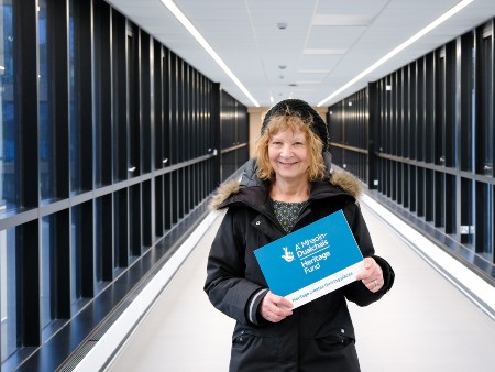 Dr Catherine Mills holds an advertising board of The National Lottery Heritage Fund