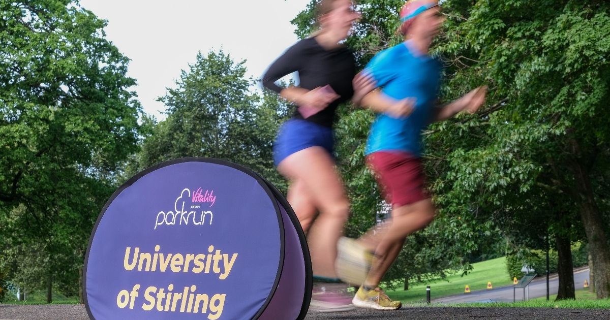Runners run by a University of Stirling parkrun banner