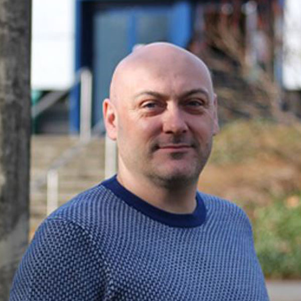 Craig is wearing a blue jumper and is stood outside.