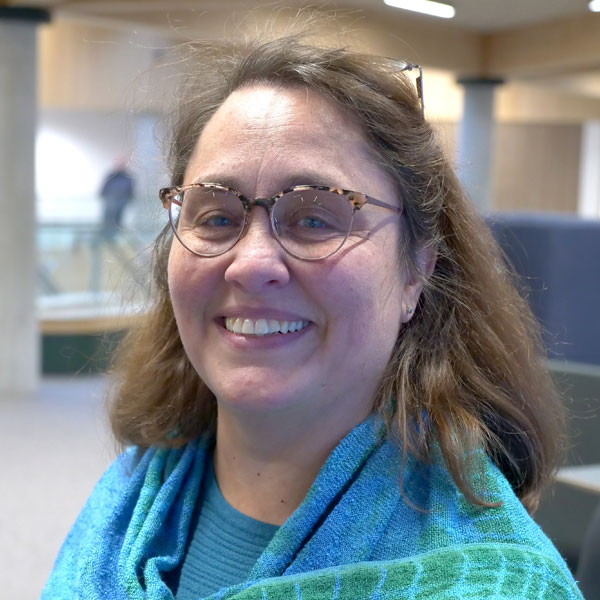 Marcelle is wearing glasses and has a blue scarf draped around her shoulders.