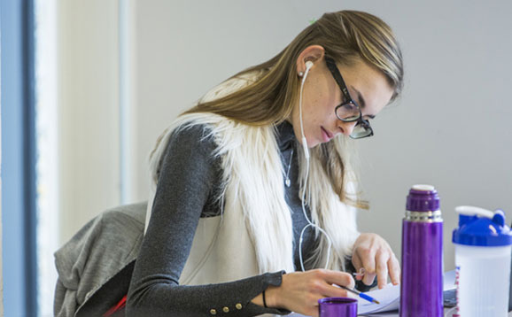 Student wearing glasses studying with earphones in