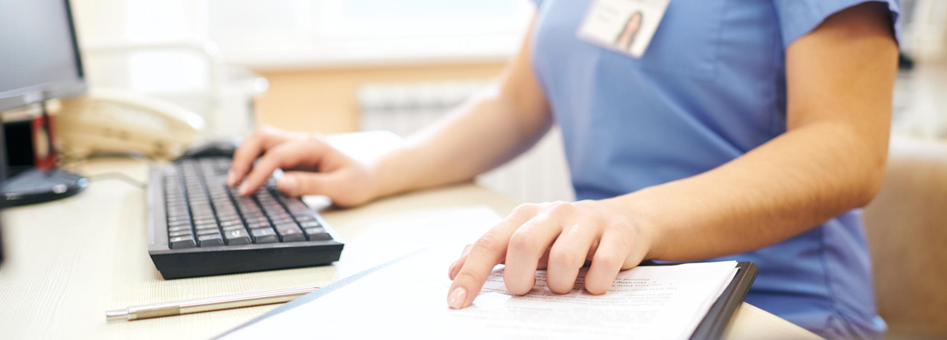 A doctor typing at a computer and referring to a notepad